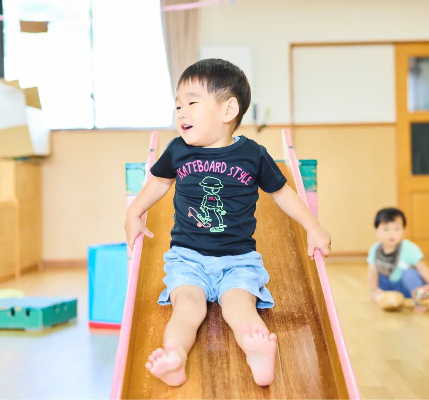 室内の滑り台の上で、笑顔の幼児が楽しそうに遊んでいる様子