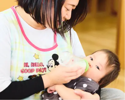 保育士が乳児を抱っこしながら哺乳瓶でミルクを飲ませている様子