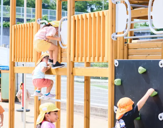 保育園の遊具で幼児たちが順番に登ったり降りたりしながら挑戦している様子