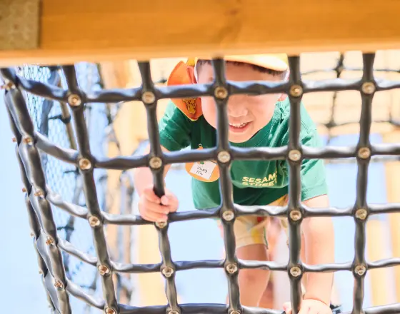 幼児が笑顔でロープネットの遊具を登っている様子