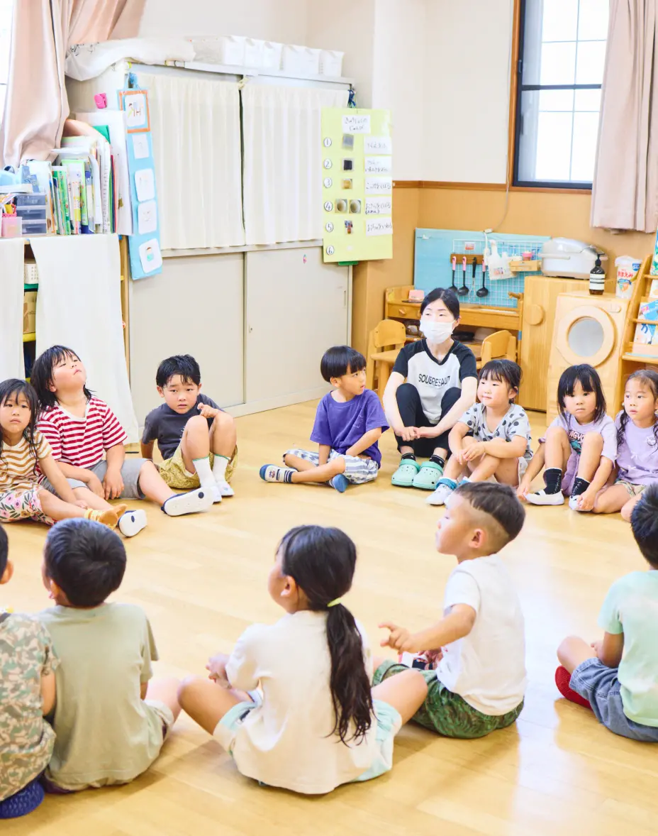 保育室で幼児たちと先生が一緒に円になって座っている様子