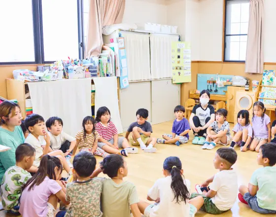 保育室で幼児たちと先生が一緒に円になって座っている様子