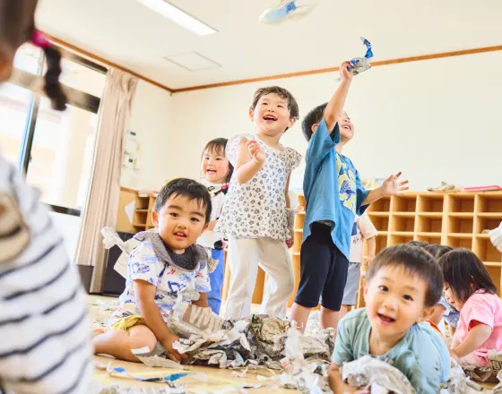 保育室で幼児たちが新聞遊びを楽しんでいる様子