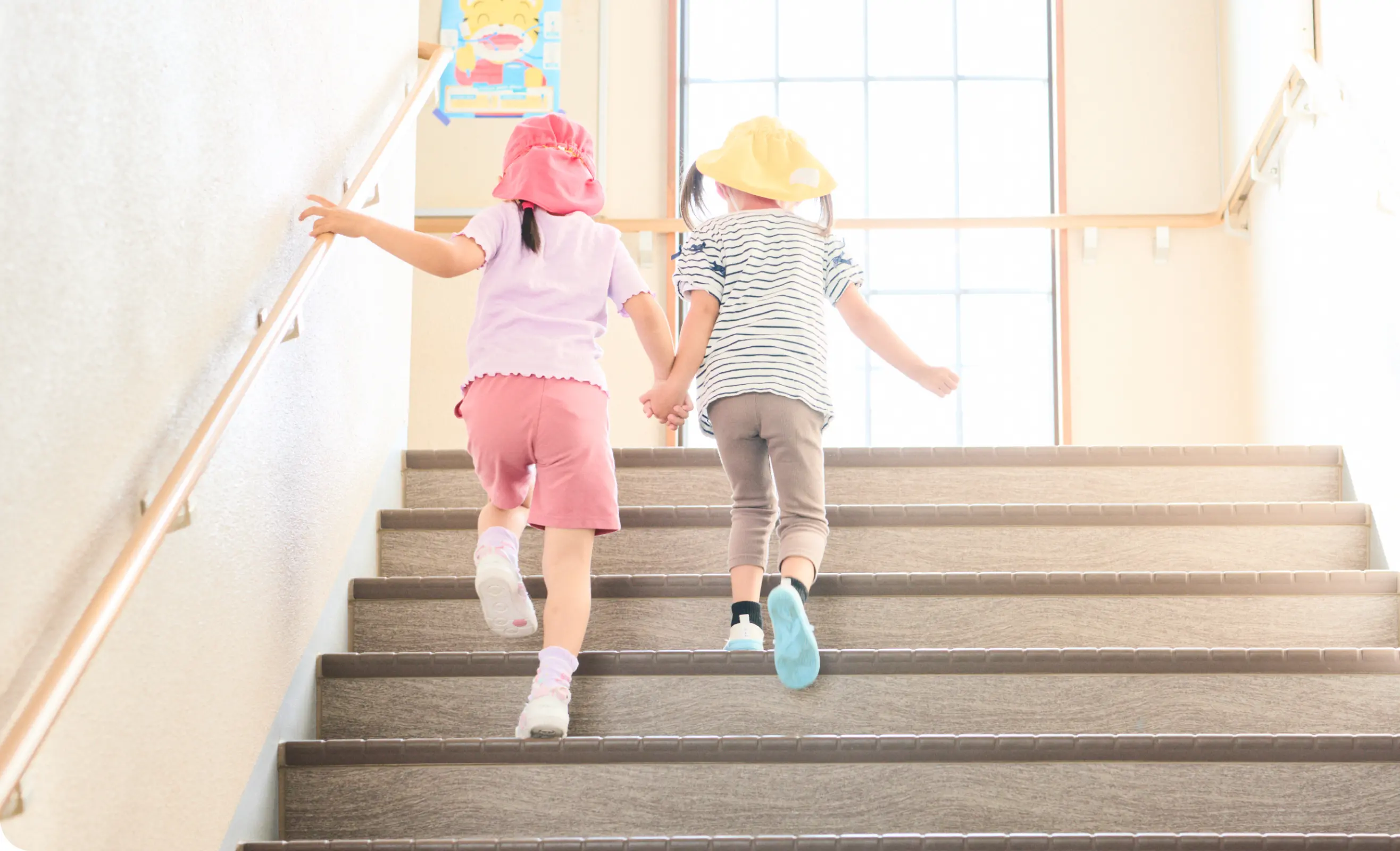 二人の幼児が手をつなぎながら階段を上っている後ろ姿