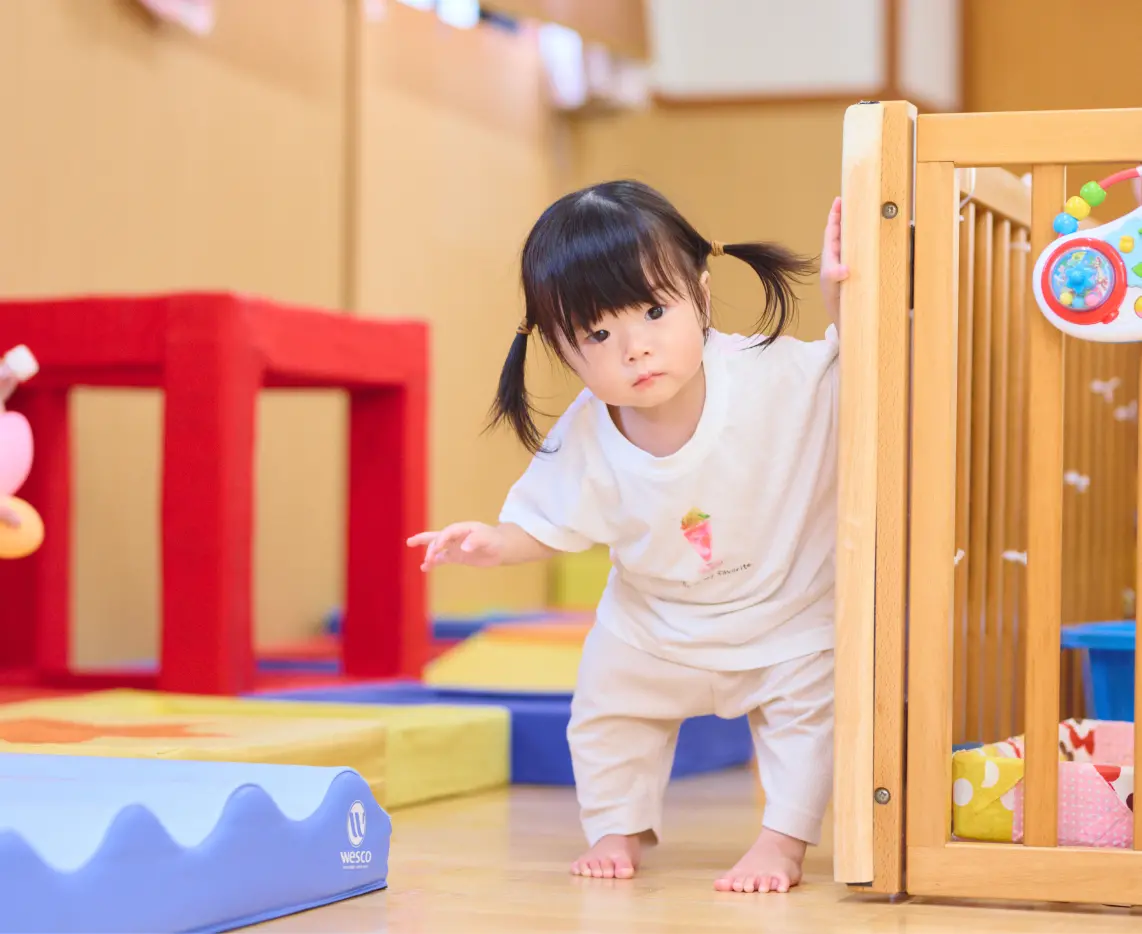 保育室で柵につかまりながら歩いている乳児の様子
