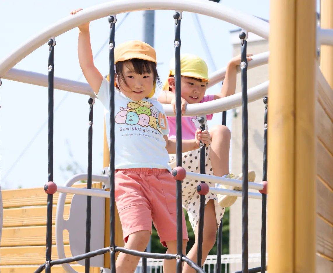 幼児たちが屋外の遊具で楽しそうに登っている様子